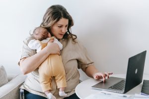 Women cradling a baby sitting in front of a laptop.