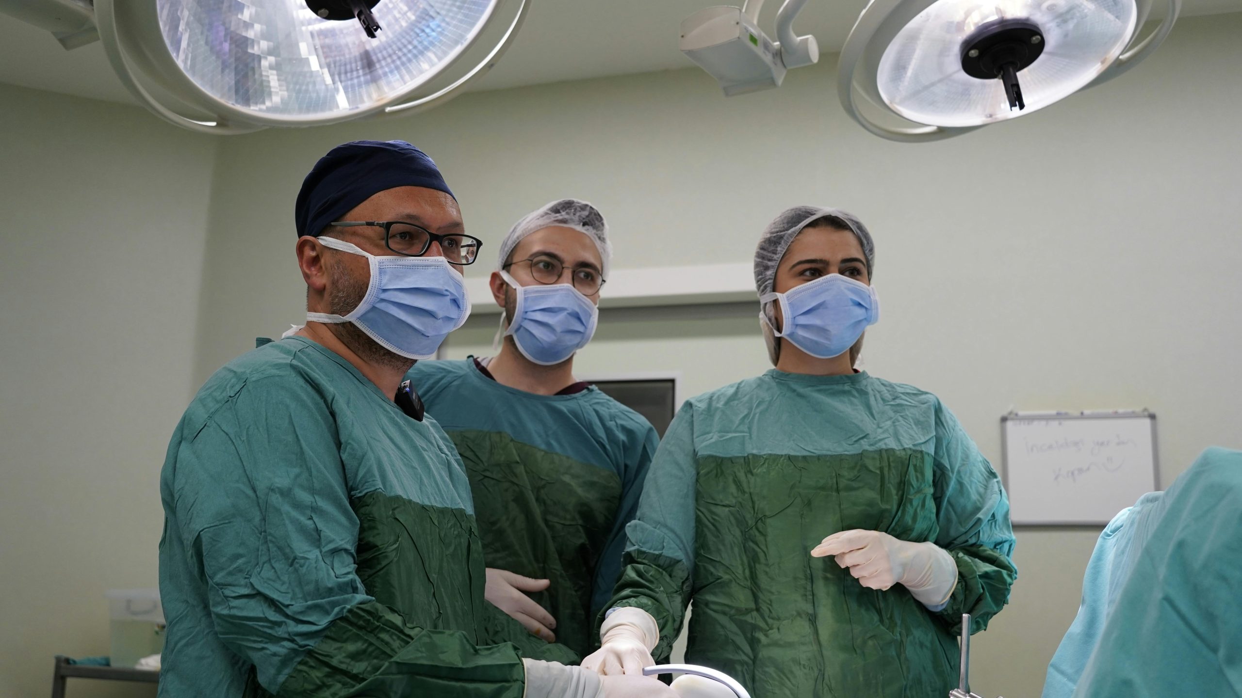 Three surgeons in sterile clothing looking at something off-camera.