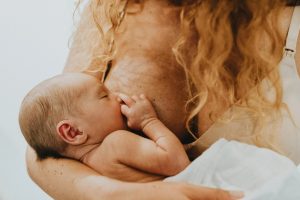 A newborn baby breastfeeds while being gently cradled by a parent with long curly hair, capturing a close and intimate moment of nourishment and bonding.